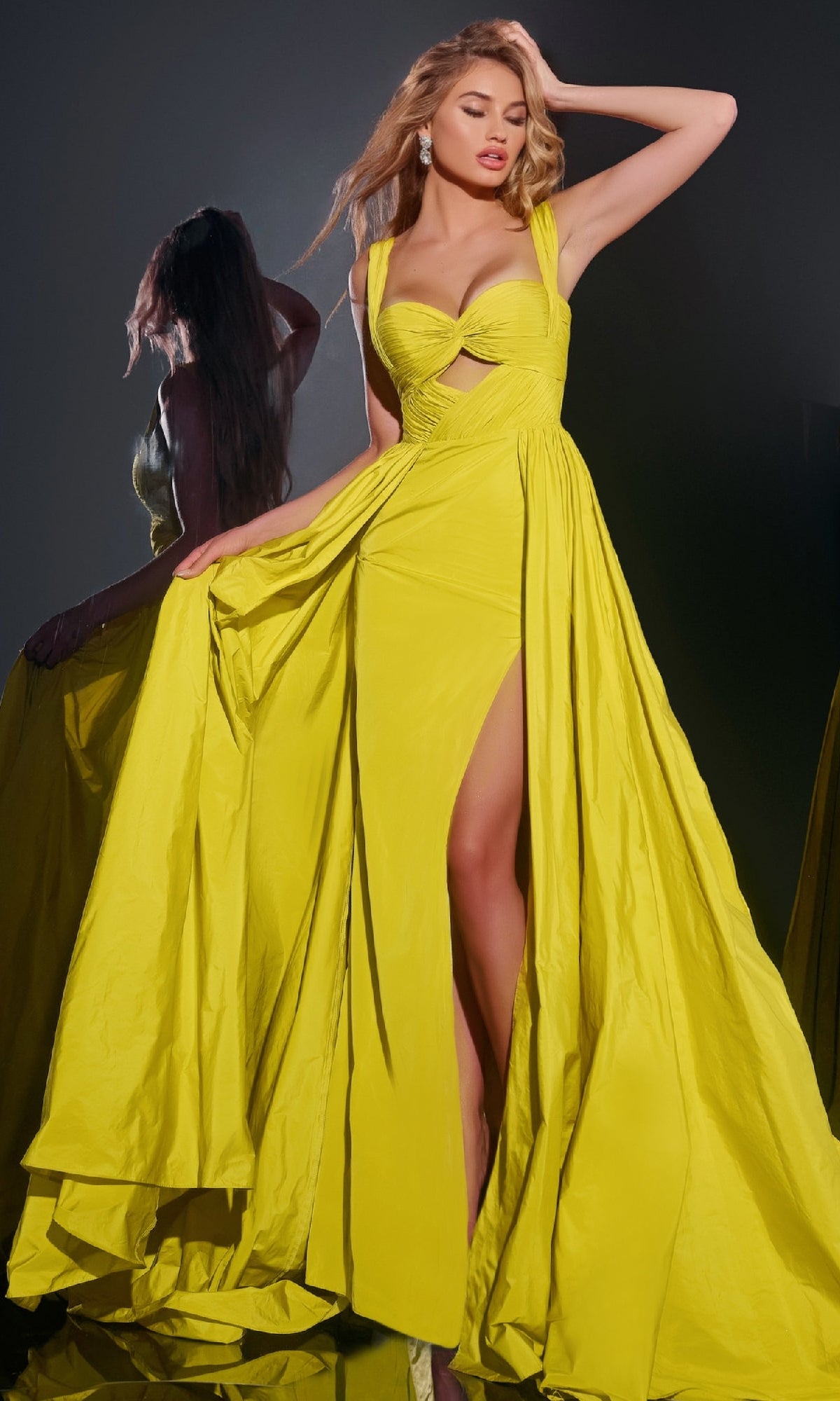 A woman poses dramatically in the Jovani 38957 long prom dress, featuring a bright yellow hue, sweetheart neckline, and high leg slit, with her reflection visible in the background.